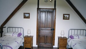 A bedroom with two single beds, wooden nightstands, a wooden door, and two wall-mounted pictures.