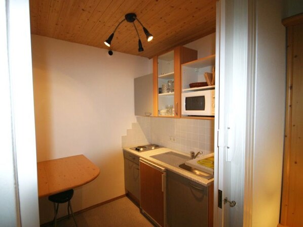 A compact kitchen with a sink, stove, and cabinets, a small table, and a ceiling light fixture.