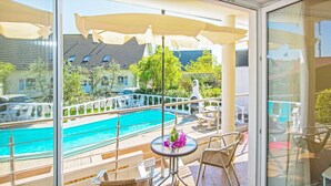 Un balcón con vistas a una piscina, mobiliario exterior y un ventanal de cristal.