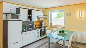 Una cocina moderna con armarios blancos, microondas y cafetera. Hay una mesa de comedor con sillas y un ventanal con vistas a zonas verdes.