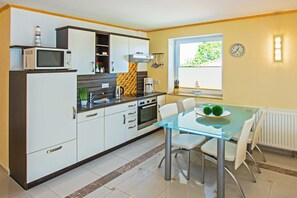 A modern kitchen with white cabinets, a microwave, and a coffee maker. There is a dining table with chairs and a window with a view of greenery.