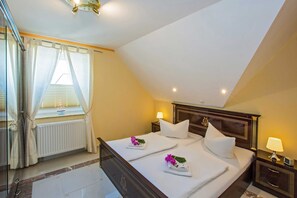 A hotel room with a bed, two bedside tables, a window with curtains, a radiator, and a ceiling light.