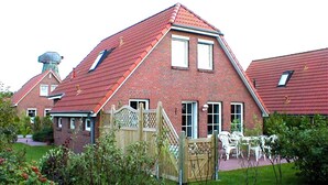 Una casa in mattoni con tetto spiovente, un cancello in legno e un giardino con piante e mobili da esterno.