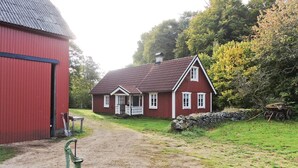 A traditional red wooden house with a porch, a stone wall, and a wooden cart. - Lovely home in Annerstad with sauna (Annerstad)