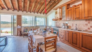 A kitchen with wooden cabinets, a dining table set for four, and a view of the outdoors through large windows. - Nice home in Caldana -GR- (Caldana -GR-)