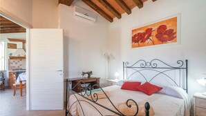 A bedroom with a metal bed frame, a wooden ceiling, a painting of flowers, and a view into the kitchen. - Nice home in Caldana -GR- (Caldana -GR-)