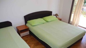 A bedroom with two single beds, wooden flooring, a nightstand with a lamp, and a window with curtains. - Holiday apartment with terrace (Crikvenica)