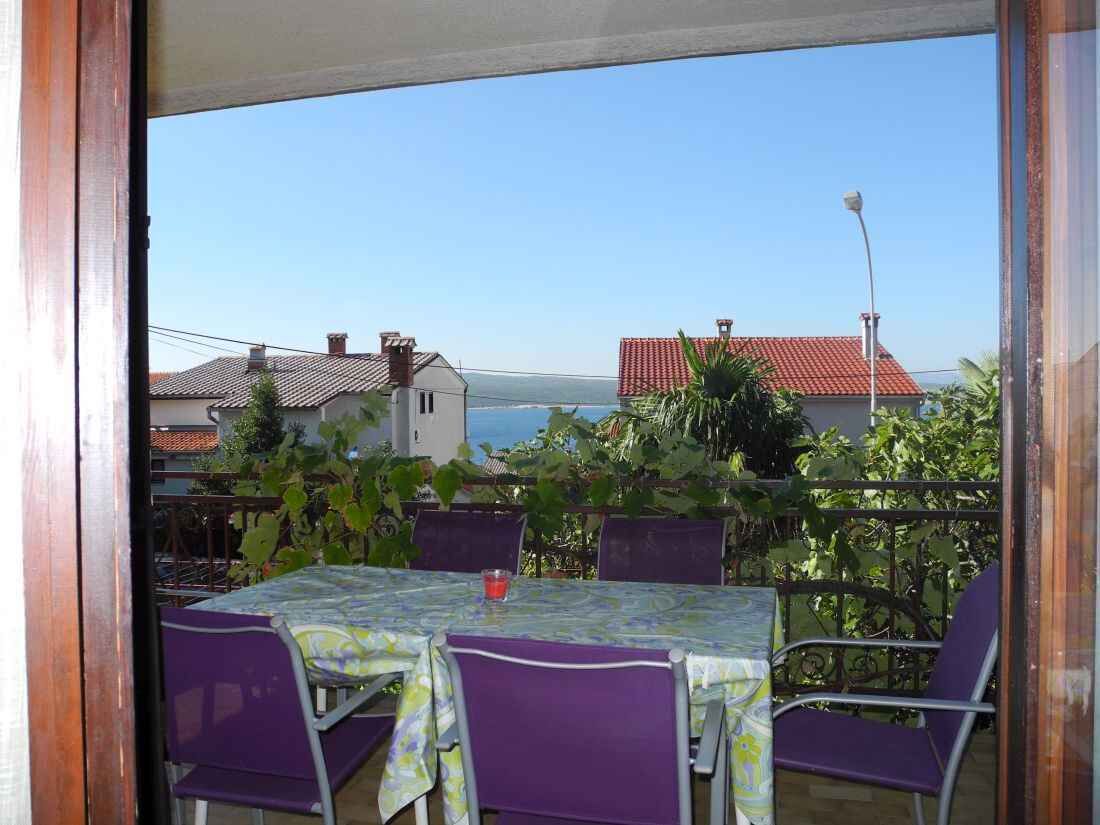 Ein Balkon mit Tisch und Stühlen, der auf eine Küstenlandschaft mit Häusern und blauem Himmel blickt.