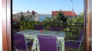 A balcony with a table and chairs, overlooking a coastal area with houses and a clear sky. - Holiday apartment with terrace (Crikvenica)