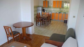 A small, compact room with a sofa, a dining table with chairs, and a kitchenette in the background. - Holiday apartment with terrace (Crikvenica)