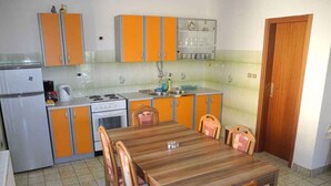 A compact kitchen with orange cabinets, a wooden dining table, and a refrigerator. - Holiday apartment with terrace (Crikvenica)