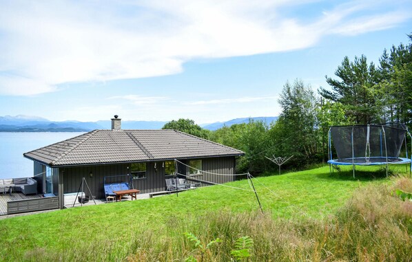 A house with a deck overlooking a lake, a trampoline, and a grassy yard.