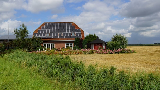 A house with a solar panel roof, surrounded by a field and a small garden with flowers. - Ferienhof Witt - Ferienwohnung Witt (Elpersbüttel)