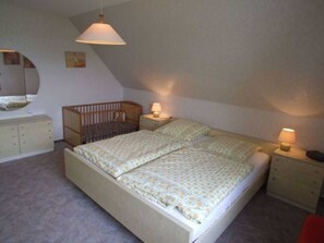 Une chambre avec un lit superposé, un berceau, une table de chevet avec une lampe et une commode.