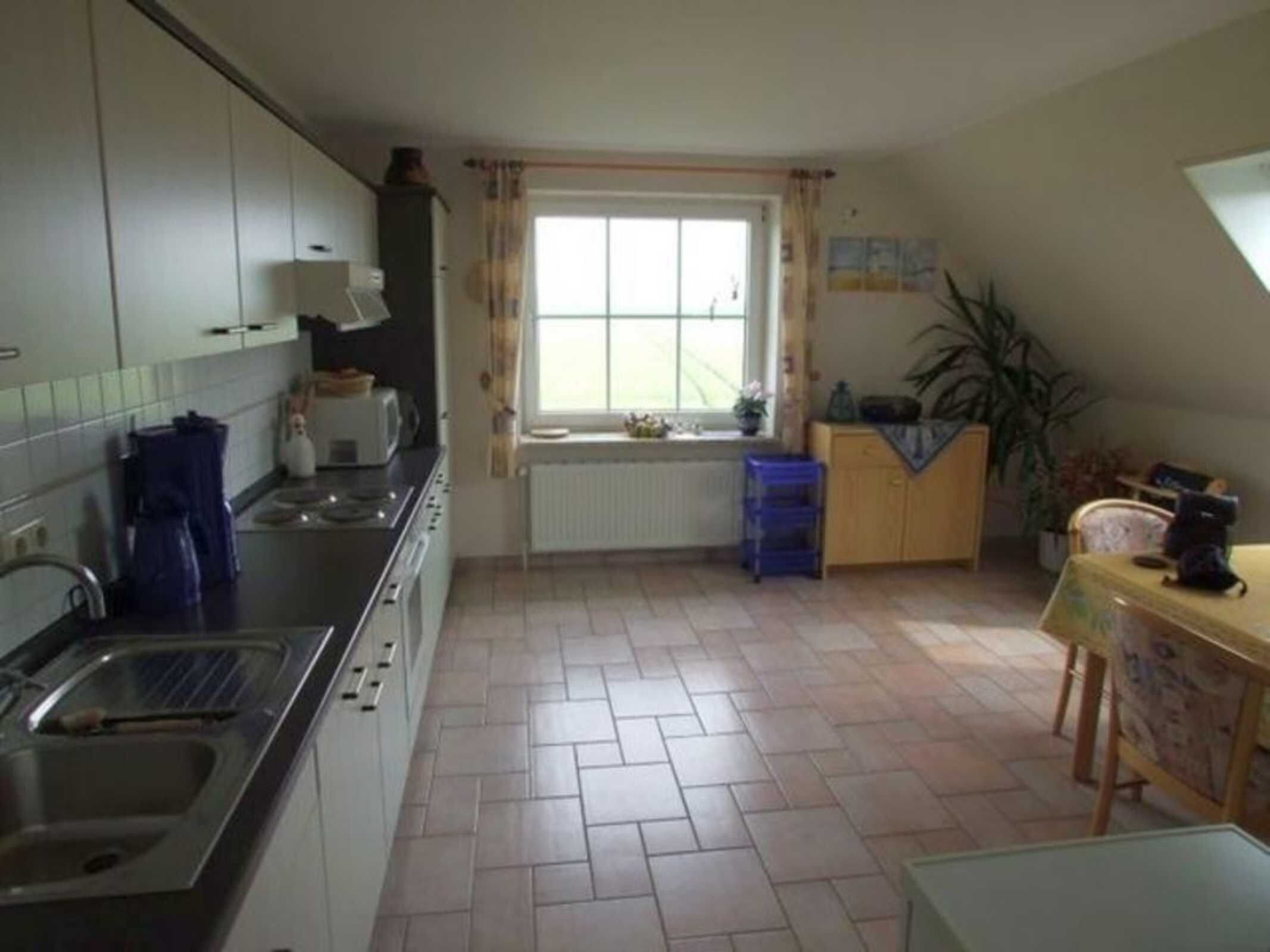 A kitchen with a stove, sink, and window. There is a radiator under the window and a blue stool near the sink.