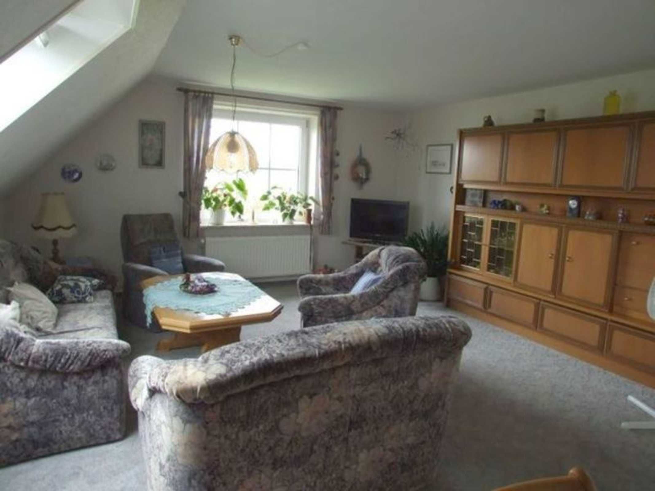A cozy living room with a sloped ceiling, a television, and a wooden cabinet.