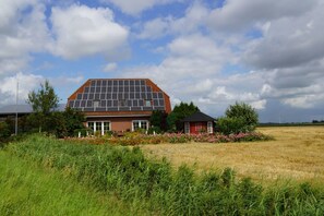 Une maison dotée d’un toit recouvert de panneaux solaires, entourée d’un champ et d’un petit jardin fleuri.