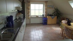 A kitchen with a stove, sink, and window. There is a radiator under the window and a blue stool near the sink. - Ferienhof Witt - Ferienwohnung Witt (Elpersbüttel)