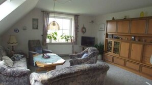 A cozy living room with a sloped ceiling, a television, and a wooden cabinet. - Ferienhof Witt - Ferienwohnung Witt (Elpersbüttel)