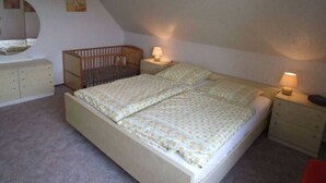 A bedroom with a bunk bed, a crib, a bedside table with a lamp, and a dresser. - Ferienhof Witt - Ferienwohnung Witt (Elpersbüttel)