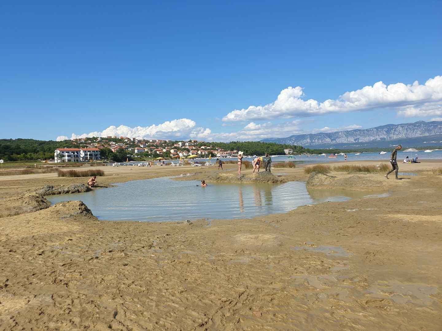 A beach with people, a body of water, and buildings in the background.