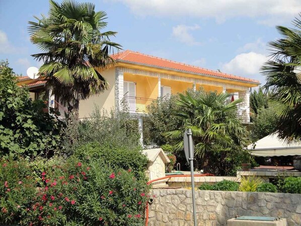 Set amidst lush greenery, this charming building boasts a two-story facade with a balcony and red-tiled roof.