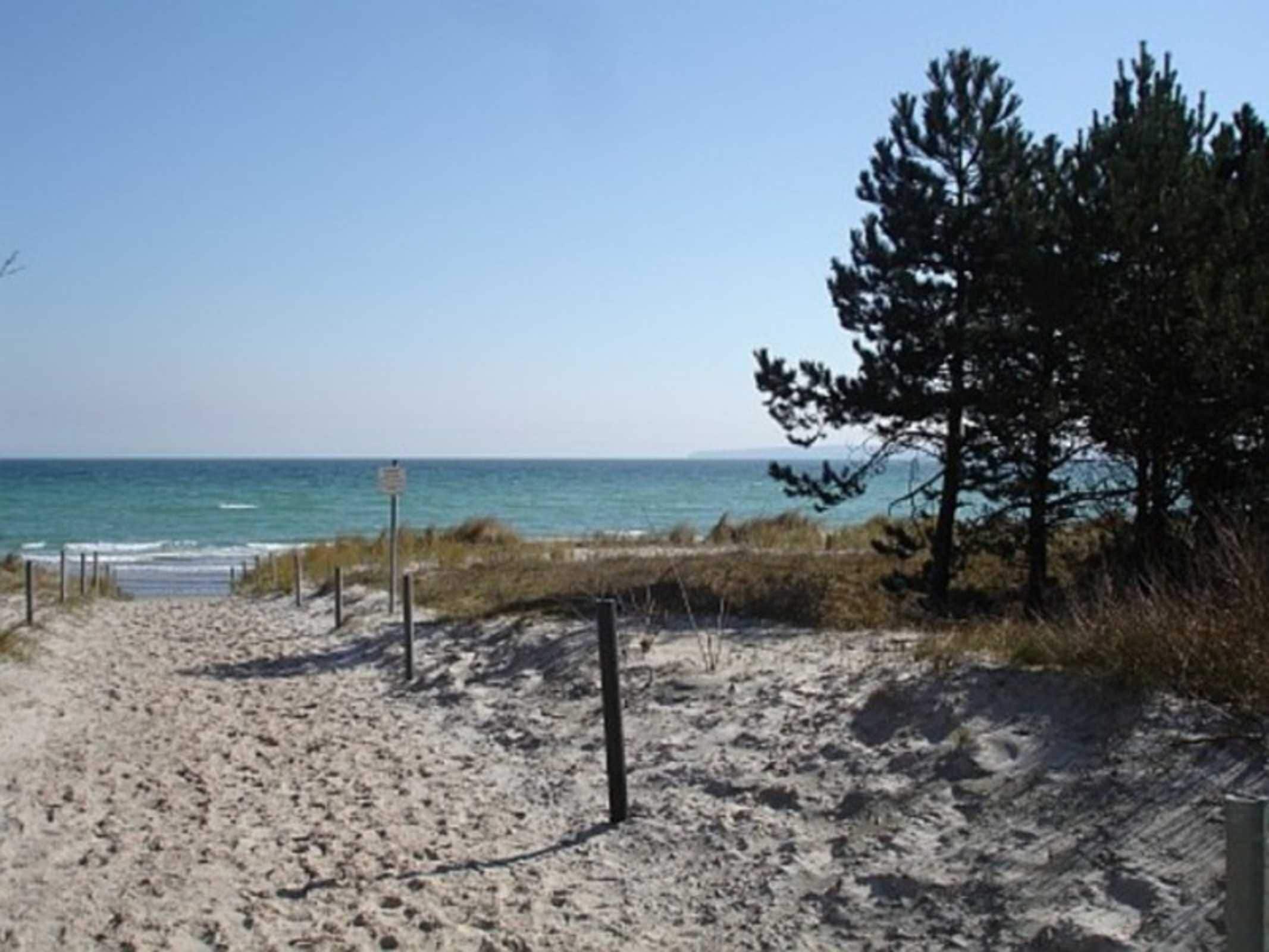 A sandy beach path leading to the ocean, with a signpost visible.