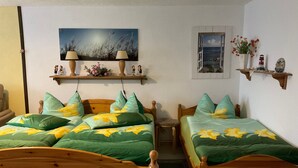 Una habitación con dos camas de madera, cada una con ropa de cama floral en tonos verde y amarillo. Sobre las camas hay un cuadro de un paisaje, y una ventana pequeña con vistas al mar.