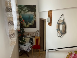 A dining area with a table set for two, a chair, a decorative plant, and a painting of a coastal scene. - Fewo UG - Rügen-Fewo 198 (Putbus)