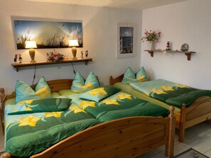 A bedroom with two wooden beds, green floral bedding, a painting above the beds, a small shelf with decorative items, and a framed picture on the wall. - Fewo UG - Rügen-Fewo 198 (Putbus)