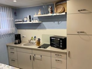 A kitchenette with a coffee maker, toaster, and knife block. There are shelves above the counter holding various kitchen items. - Fewo UG - Rügen-Fewo 198 (Putbus)
