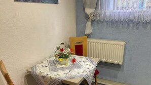 Un comedor con una mesa cubierta con mantel floral, un jarrón con flores y una silla con cojín rojo.