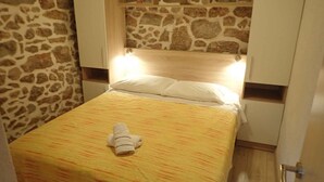 A neatly made bed with a towel, a stone wall, and wooden cabinets. - Holiday home mit Klimaanlage und Terrasse (Starigrad-Paklenica)