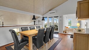 Un comedor con una mesa de madera y sillas negras, un techo con vigas de madera y vista a una piscina a través de puertas de cristal.
