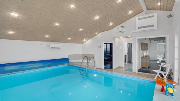 Una piscina interior con techo de madera, un jacuzzi y un vestuario con ducha.