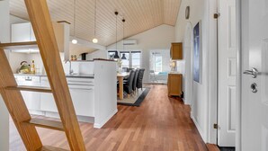 Una cocina moderna con armarios blancos, techo de madera y comedor con mesa y sillas.