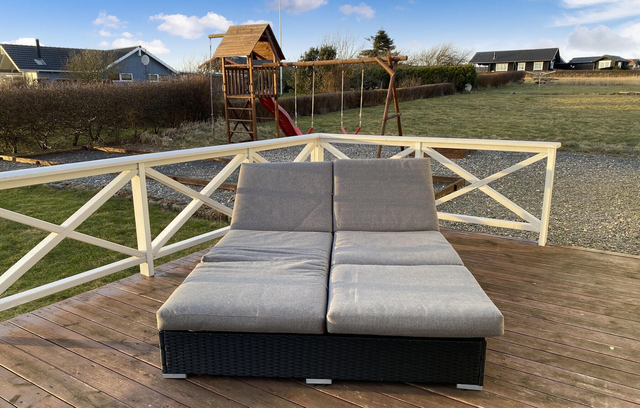 Een terras met een bank en een schommelset in de achtergrond.