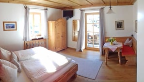 A bedroom with a bed, a wooden wardrobe, a television, a table with a vase, and a bench.