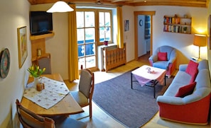 Ein gemütliches Wohnzimmer mit Sofa, Esstisch mit Stühlen, Fernseher und Bücherregal.
