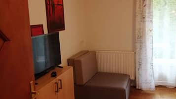 Une pièce comprenant un meuble en bois, une télévision, un canapé, un radiateur et une fenêtre avec des rideaux.