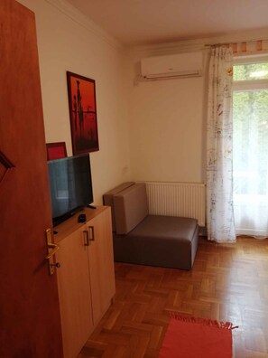 Een kamer met een houten kast, een televisie, een bank, een radiator en een raam met gordijnen.