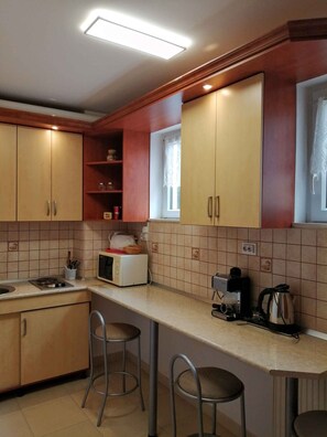 Een kleine keuken met houten kastjes, een magnetron, een broodrooster en een waterkoker. Er staan twee krukken bij het aanrecht.