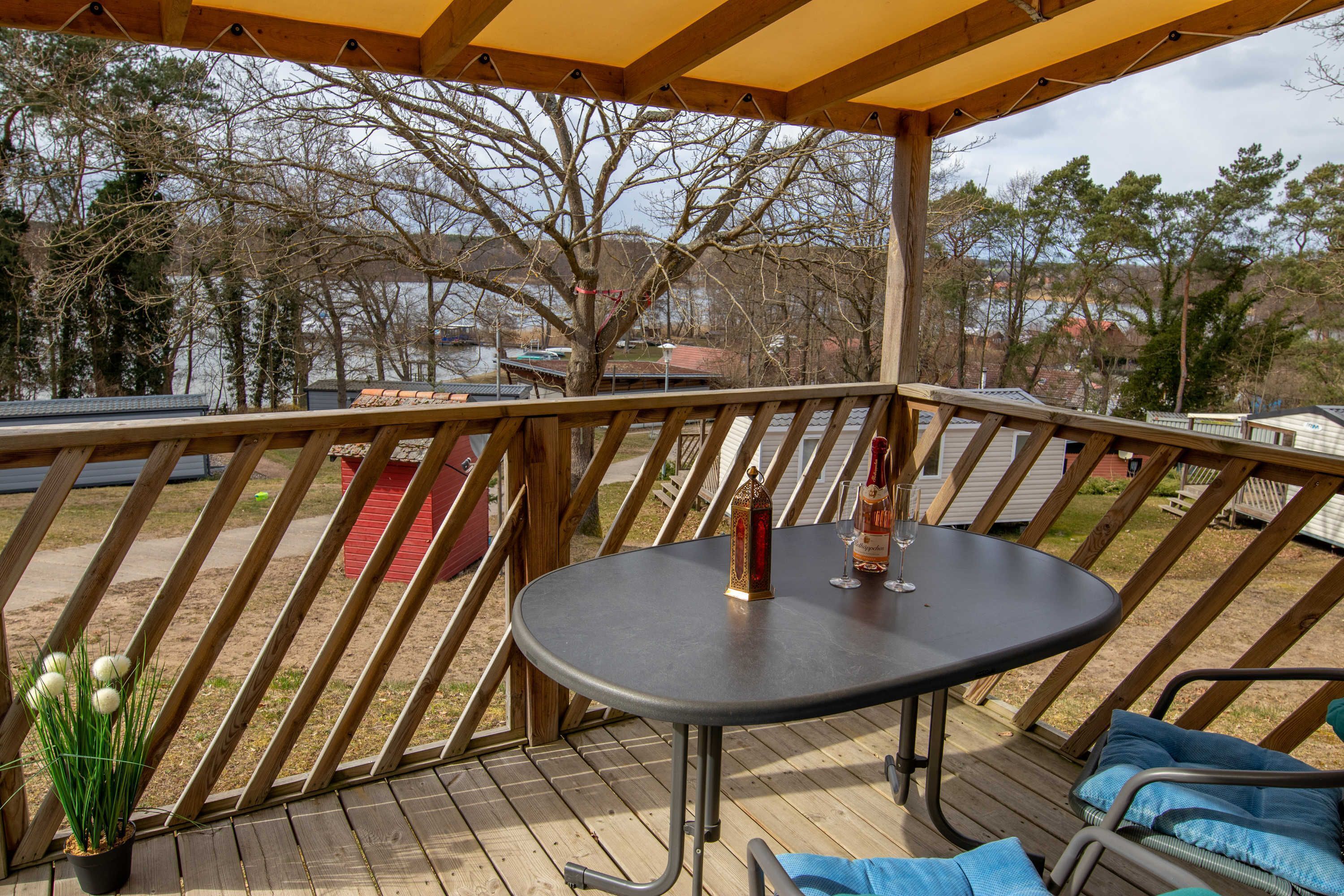 Una terraza cubierta al aire libre con una mesa y sillas, con vistas a un cuerpo de agua y árboles.