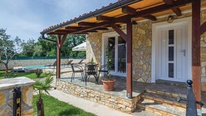 Un área de patio techada con muros de piedra, una piscina y mobiliario exterior.