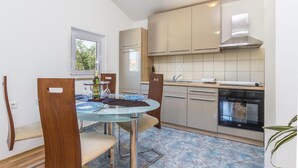 Cocina compacta con zona de comedor, que incluye una mesa de vidrio, sillas de madera y horno empotrado.