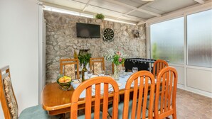 Un comedor con pared de piedra, televisor de pantalla plana, dardos y mesa de fútbol de mesa.