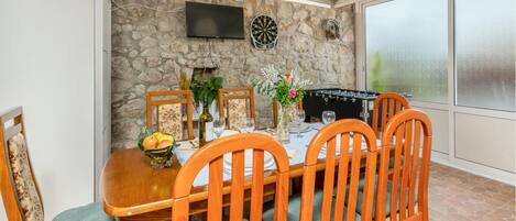 Un comedor con pared de piedra, televisor de pantalla plana, dardos y mesa de fútbol de mesa.