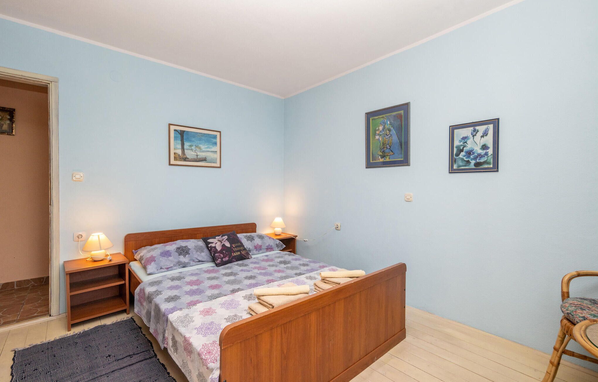 A bedroom with a wooden bed, two bedside lamps, a small shelf, and two framed artworks on the wall.