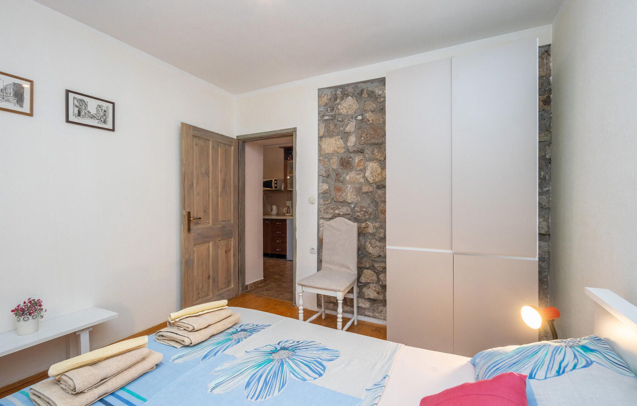 Ein Schlafzimmer mit einem Bett, einem Sessel, einem kleinen Tisch mit Handtüchern und einer Steinwand.