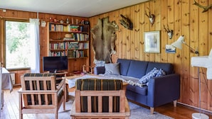 Un'accogliente camera in stile baita, con arredamento in legno, un divano blu, due sedie di legno, una televisione, una libreria e diverse decorazioni murali tra cui pelli di animali e corna di cervo.